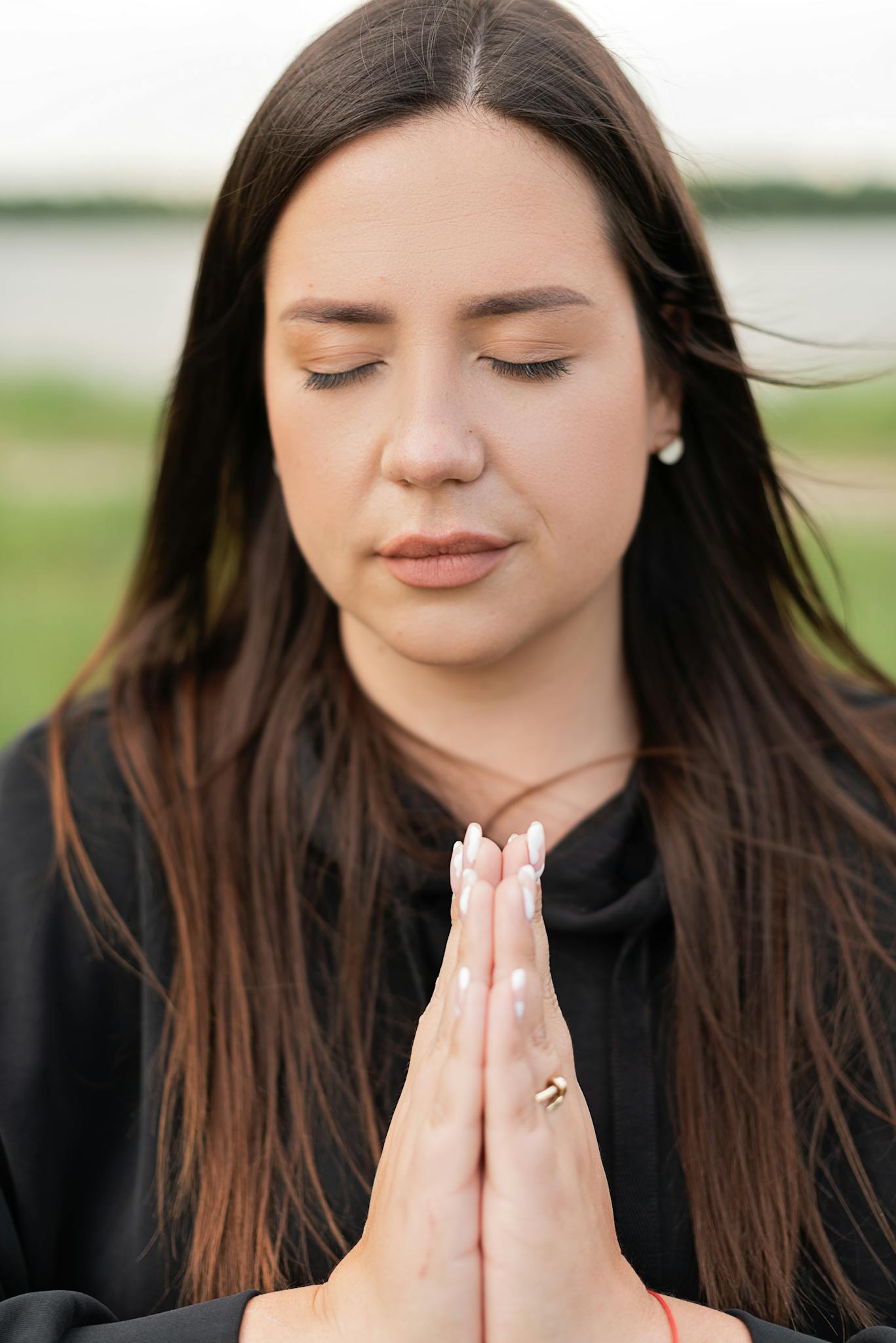 Close-up of a woman meditating with eyes closed, hands in prayer, outdoors in a park.