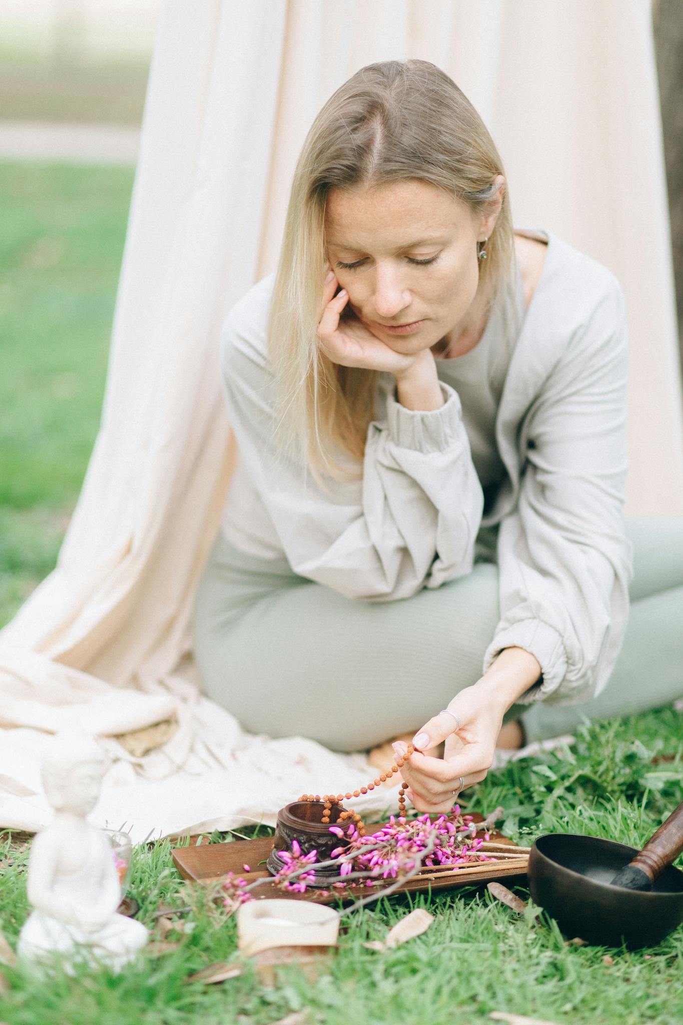 Woman in meditation with flowers and beads, embracing tranquility in nature.